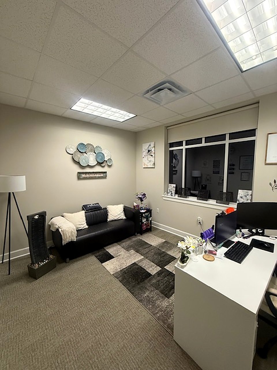 A consultation room with a black leather sofa and a floor lamp